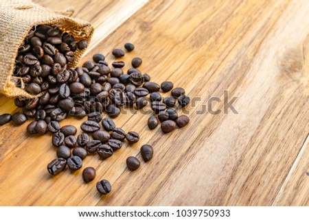 Roasted coffee beans in a sack are placed on a wooden floor. Some coffee beans are on the floor. Close up view of coffee beans. Photo taken with natural light