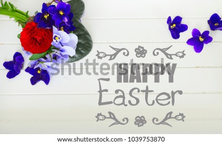 Posy of violets, pansies and ranunculus on white wooden background with happy Easter greeting