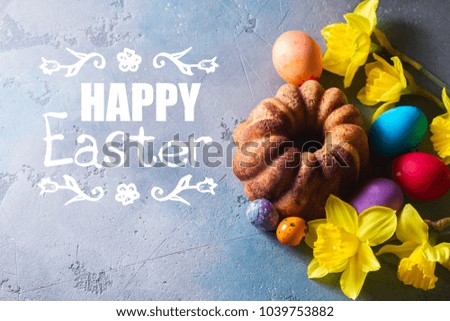 Easter cake, yellow flowers with colored eggs on gray background, top view with happy Easter greeting
