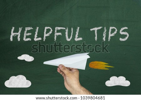 Hand holding paper plane and Text Helpful Tips written on green blackboard