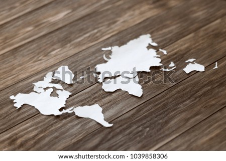 World map cutted from white paper on the wooden background. Close-up, soft focus, copy space, mock up, diagonal arrangement