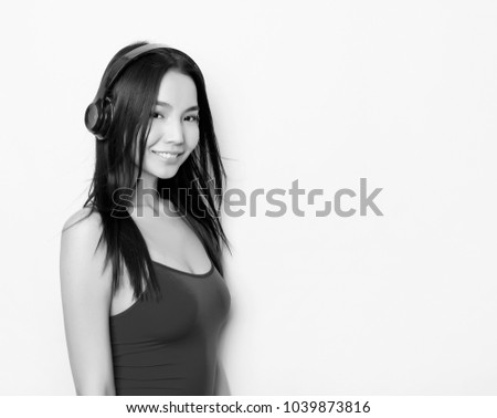 beautiful young asian woman with long hair wearing red tank top and listening to music with headphones on grey background with copy space