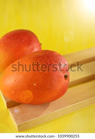 Two ripe mangoes on wooden boards on bright yellow background