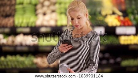 Caucasian woman grocery shopping taking photo of nutrition label of can of beans