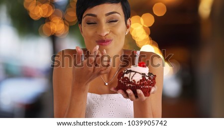 Smiling black female eating fancy cupcake in outdoor setting with bokeh lights Royalty-Free Stock Photo #1039905742