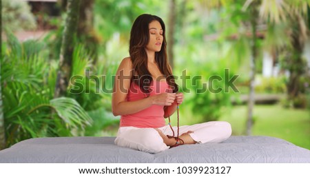 Young Latina woman with serene expression meditating with prayer beads outdoors Royalty-Free Stock Photo #1039923127