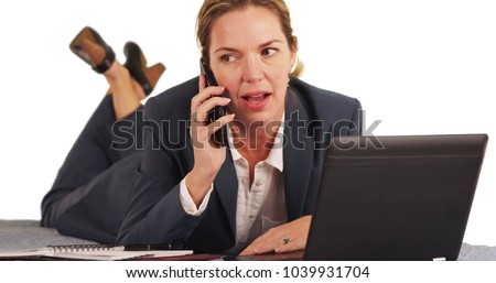 Businesswoman lying on stomach answering phone call and working on laptop 