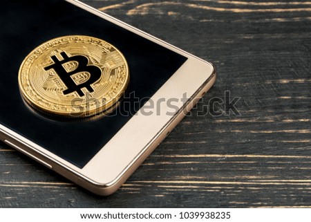 Part of the smartphone with a gold coin bitcoin on the table