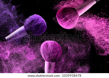 Three brushes for makeup with pink and purple make-up shadows in motion on a black background.