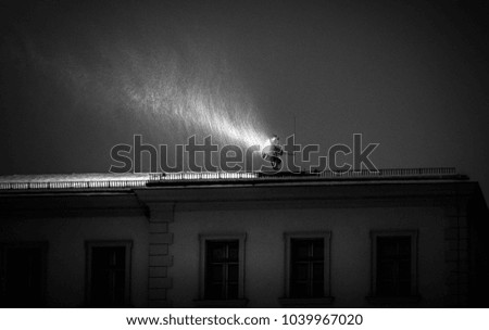 Black and White Picture with a spotlight in Top of a roof in a Snow Storm 