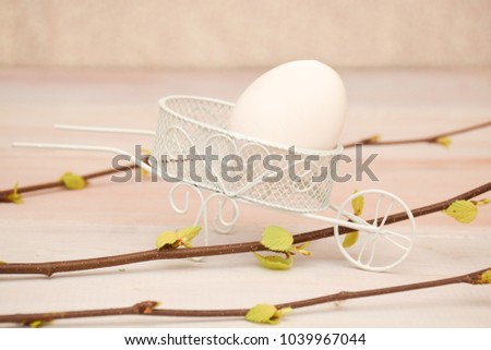 Easter picture. A white chicken egg lies in a cart. A trolley in the style of Provence. Branches of birch with fresh foliage. Shield of wooden light boards