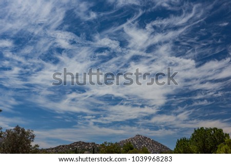 Wispy clouds above mountain and trees.