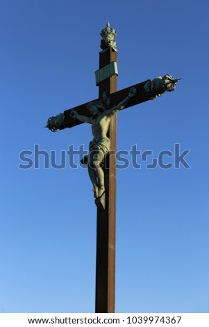 Close up outdoor view from below of a cross with jesus christ. Isolated religious symbol with blue vivid sky in background. Sculpture lighted by the sun. Symbolic abstract image taken in a french city