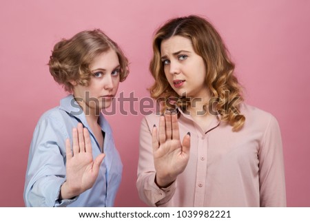 two young girls in protest reach out in front of them and demand to stop and stop. The concept of disagreement, refusal and protest. Studio portrait on a pink background Royalty-Free Stock Photo #1039982221