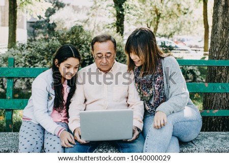 
A father with his daughters sitting on a stone bench, learning to use the laptop. Relaxed autumn day in family outdoors. Lifestyle portrait.

