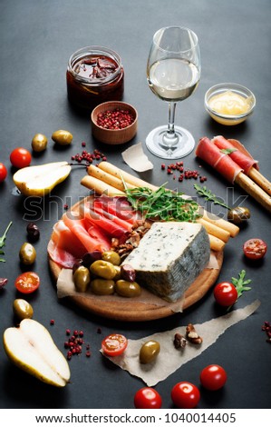 Mediterranean products (ham, blue cheese, arugula, cherry, nuts) on a brown cutting board. Dark background. Useful natural fresh food