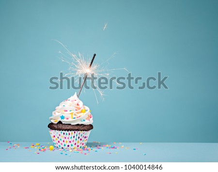 Cupcake with sprinkles and a sparkler over a blue background.