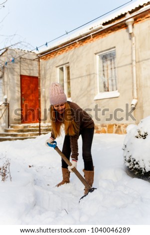 Woman shoveling and removing snow in front of her house in the suburb.
