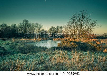 Golden dawn light breaks on a frozen pond on Wetley Moor, Staffordshire. A stark contrast to the frozen moorland that is still in shadow.