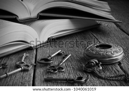 Black and white image of two open books and vintage keys on an old wooden desk top. 