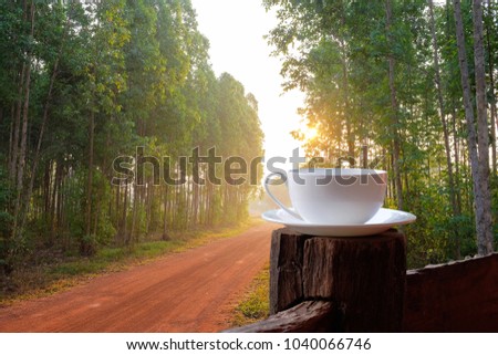 a selective focus picture of a cup of coffee on wooden fence house terrace beside rural road in summer of Thailand.  