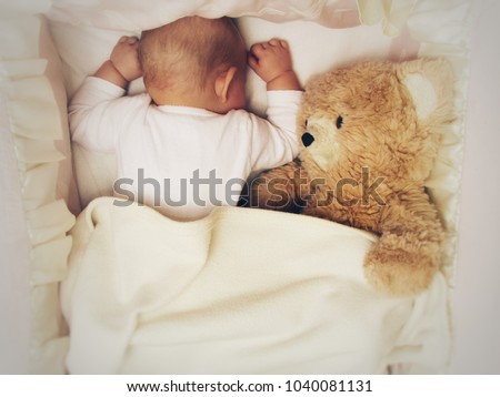 cute baby sleeping with a teddy bear in the crib under the blanket