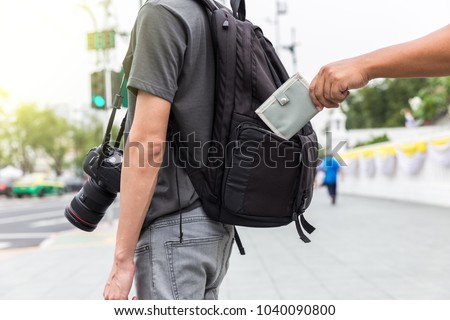 closeup pickpocket's hand stealing purse from backpacker Royalty-Free Stock Photo #1040090800