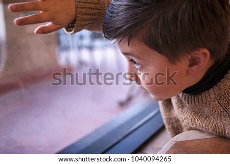 mixed race Asian Caucasian little boy with brown hair wearing brown sweater gazing out a window on a rainy day