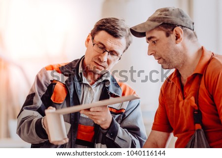Carpenter working on woodworking machines in carpentry shop. Toned image. Man collects furniture boxes. Consults with a colleague Royalty-Free Stock Photo #1040116144
