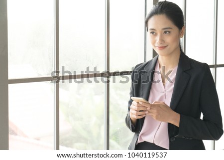 Business woman wearing suit, looking smartphone. Open space loft office. Panoramic windows background