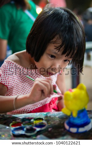 Blurred Asian pretty girl child painting watercolor on doll in market street festival holiday.