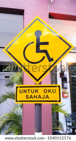 Reserved parking for Handicapped Only sign with Malaysian language "parking for handicapped only" beneath. Handicap sign on yellow background.