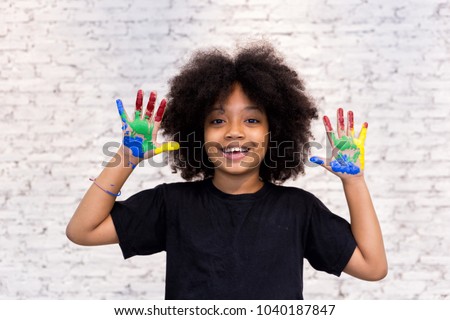 African American playful and creative kid getting hands dirty with many colors - in white brick background