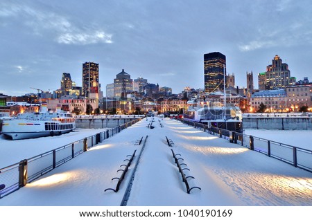 Snow-covered benches, pier, waterfront walkway, harbor, and downtown Montreal after sunset in winter - Montreal, Canada