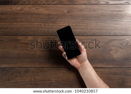 Female hands using a smartphone on a wooden table.
