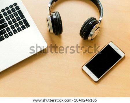 Equipment for work communication such as laptop, headphone, and smartphone on wood table.