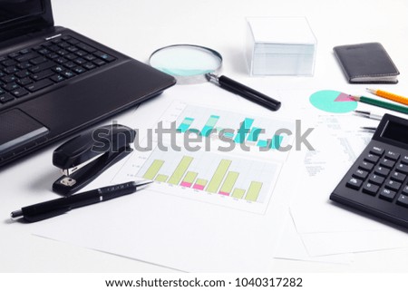 Part of laptop, calculator, diagrams, graphs, documents, pen, glasses and magnifier, pencils on white background