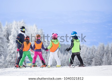 Group of kids learning how to ski on slope with instructor. Blue sky and white firs in background