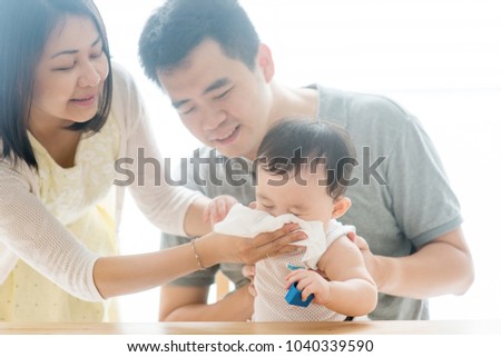 Mother wipes baby nose with tissue paper. Asian family spending quality time at home, living lifestyle indoors. Royalty-Free Stock Photo #1040339590