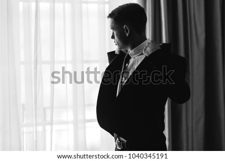 Black and white picture of handsome groom standing before a mirror in the morning