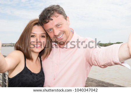 Happy young couple taking photos using mobile smart phone camera inear city river - Travel lovers making selfie portrait for social media network