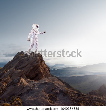 Futuristic astronaut on the planet, standing on top of a mountain and stretches his hand away Royalty-Free Stock Photo #1040356336
