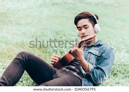 Asian young men lie about on nature listen to music with headphone and play ukulele