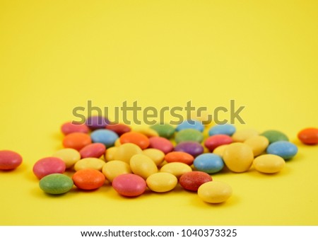 Colorful lentils stock images. Colorful candies on a yellow background. Chocolate lentils snack