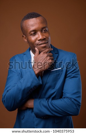 Studio shot of young African businessman wearing blue suit against brown background