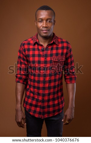 Studio shot of young African man wearing red checkered shirt against brown background