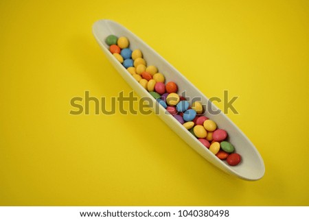 Colorful lentils stock images. Colorful candies on a yellow background. Chocolate lentils snack. Colorful candy in a white bowl