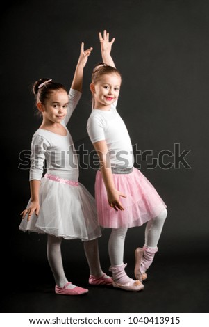 Small pretty ballerinas posing at studio, on black background