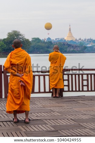 Buddhist monks looking at the Shwedagon Pagoda and the Mingalarbar Hot Air Balloon from the Kandawgyi Lake. In Yangon, Myanmar