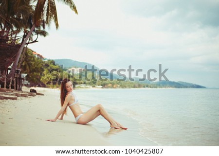 side view of young woman in bikini resting on beach near ocean